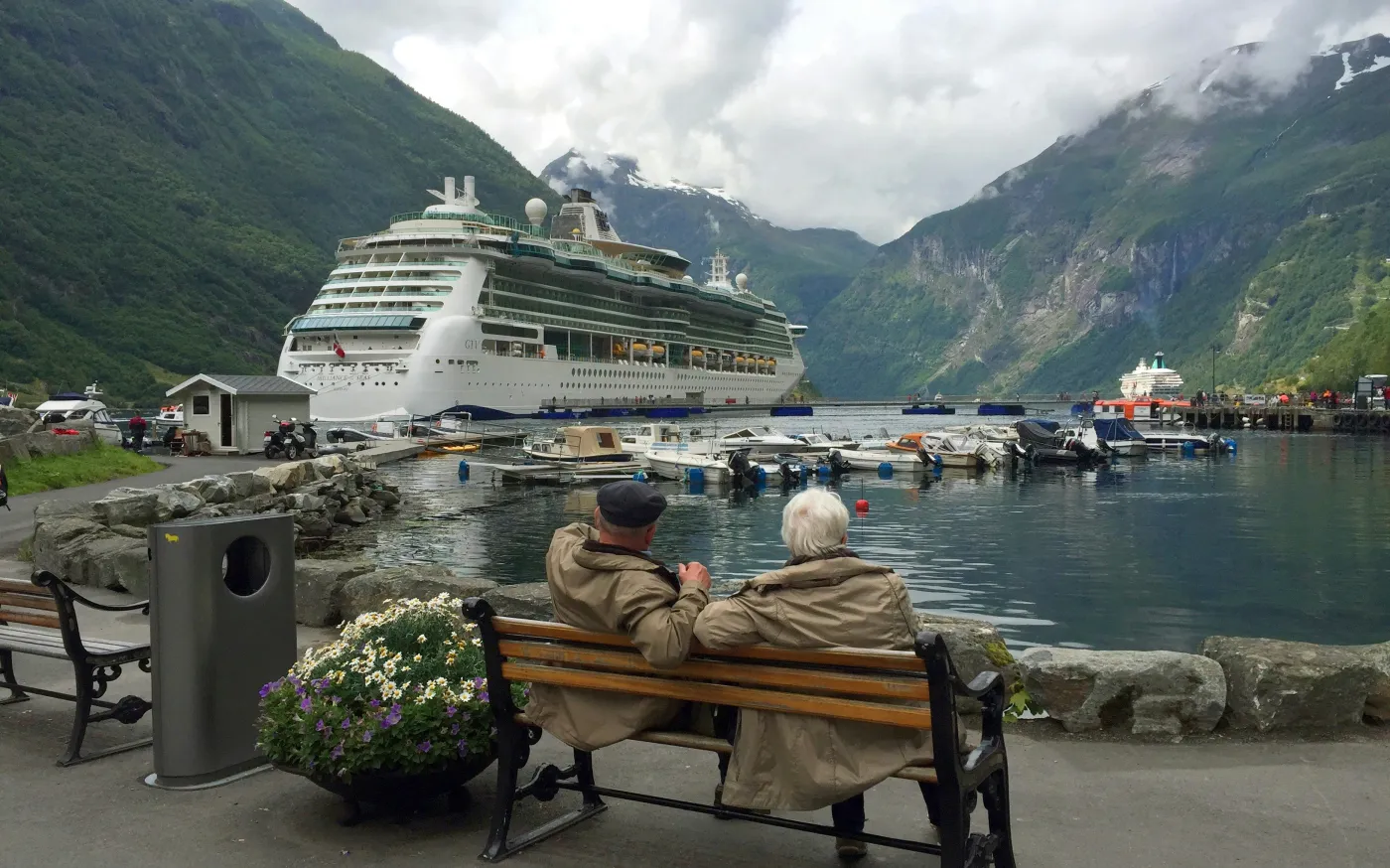 woman in brown coat sitting on brown wooden bench near white cruise ship during daytime by Julius Yls courtesy of Unsplash.